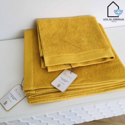 Três toalhas amarelas empilhadas com etiquetas e logótipo ao fundo