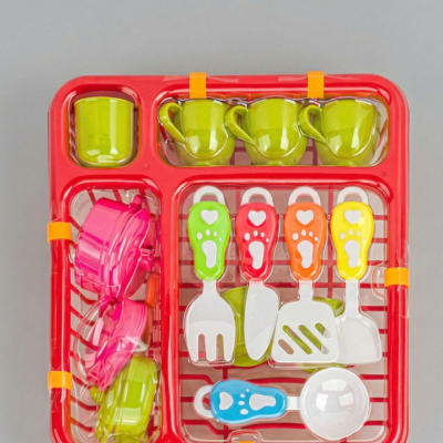 Conjunto de loiça de brincar com chávenas verdes, tachos rosa e verde, utensílios coloridos num tabuleiro vermelho.