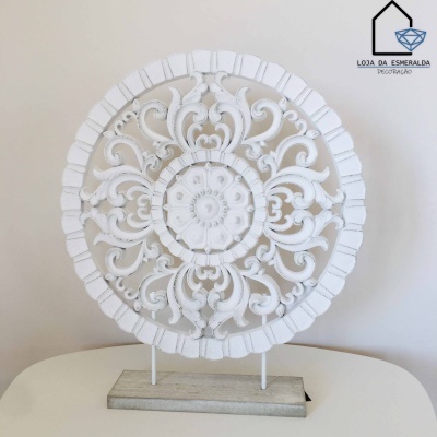 Ornamento decorativo redondo branco com padrões florais em madeira sobre mesa branca