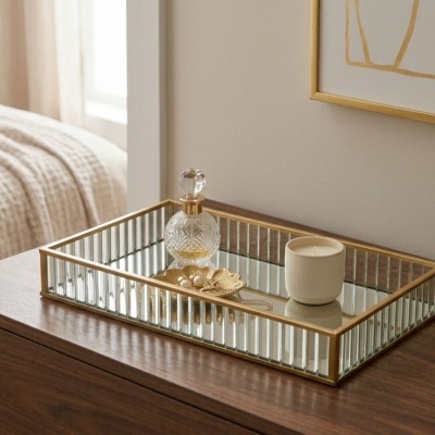 Bandeja espelhada com frasco de vidro, vela branca e prato dourado com joias