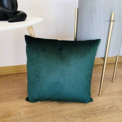 Almofada verde escura com padrão geométrico no chão ao lado de mesa e vaso.