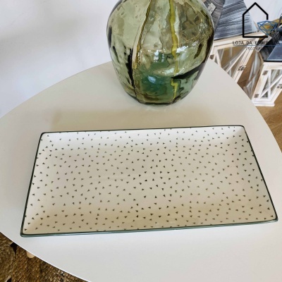 Placa retangular de cerâmica com padrão de triângulos pretos sobre fundo branco e vaso verde ao lado