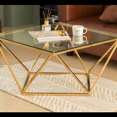 Mesa de centro com tampo de vidro e estrutura metálica dourada em sala com sofá castanho