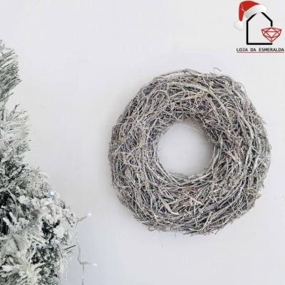 Guirlanda de ramos secos acinzentados pendurada numa parede branca ao lado de árvore de Natal com neve artificial