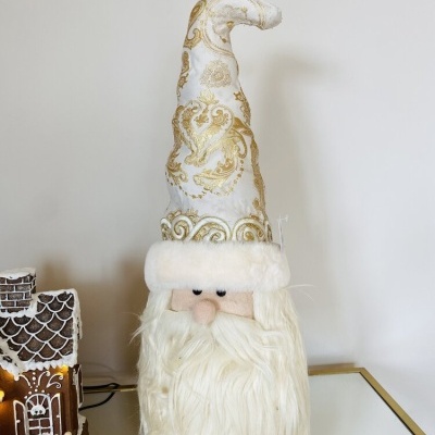Figura decorativa de Pai Natal com chapéu alto branco e dourado e barba longa branca numa mesa branca
