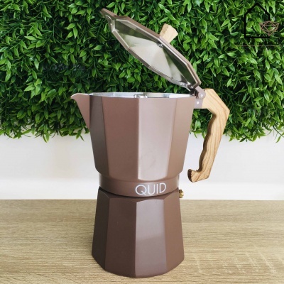 Cafeteira italiana castanha com pega de madeira sobre mesa clara e fundo de folhas verdes