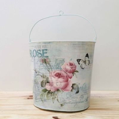 Balde metal decorativo com rosas e borboleta sobre madeira