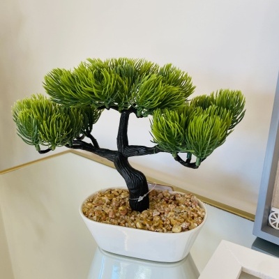 Árvore artificial em vaso branco com pedras sobre superfície espelhada
