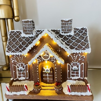 Casinha decorativa estilo gingerbread com luzes LED amarelas, detalhes em branco, castanho e vermelho.