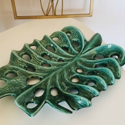 Prato decorativo de cerâmica verde em forma de folha com buracos sobre mesa branca