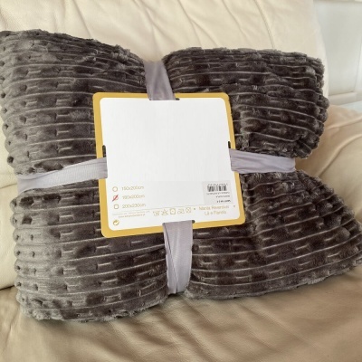 Manta cinzenta texturizada com etiqueta e fita cinzenta sobre sofá bege