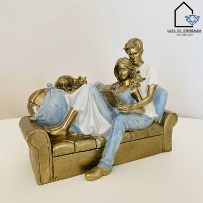 Escultura de casal sentado num sofá com gato e almofada, cores castanho dourado, azul e branco.
