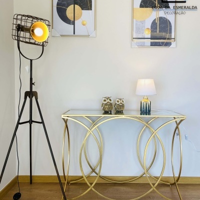 Consola dourada de vidro com esculturas de coruja, candeeiro de mesa e de pé, e quadros geométricos na parede