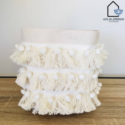 Cachepot bege com franjas e pompons sobre mesa de madeira clara