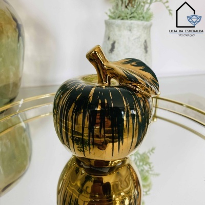 Maçã decorativa dourada e preta com folhas numa superfície espelhada