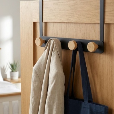 Cabide metálico com ganchos de madeira numa porta com casaco e bolsa pendurados