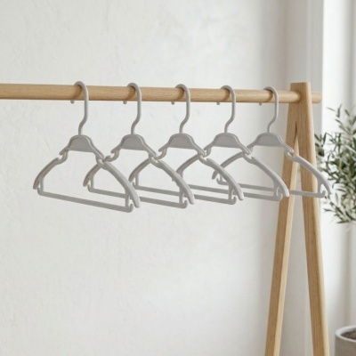 Cinco cabides cinza claro em plástico pendurados em cabideiro de madeira clara