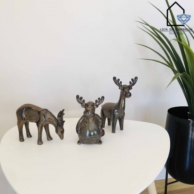 Três esculturas decorativas de veados em metal castanho numa mesa branca ao lado de uma planta