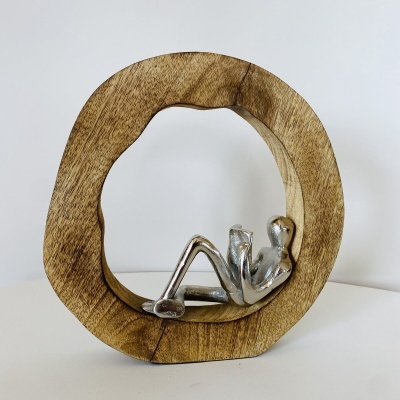 Escultura decorativa com estrutura circular de madeira e figura humana metálica prateada reclinada