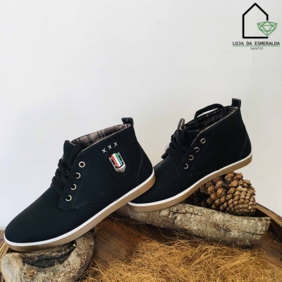 Sapatos pretos tipo ténis com sola branca e brasão colorido sobre troncos de madeira