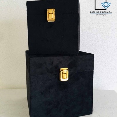 Caixas pretas de veludo com fechos dourados empilhadas com logótipo na parede atrás.