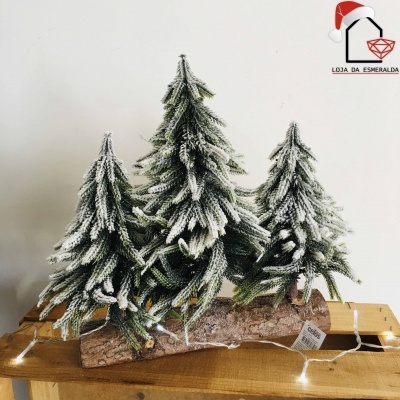 Três árvores de Natal artificiais com neve sobre tronco de madeira numa mesa de madeira clara