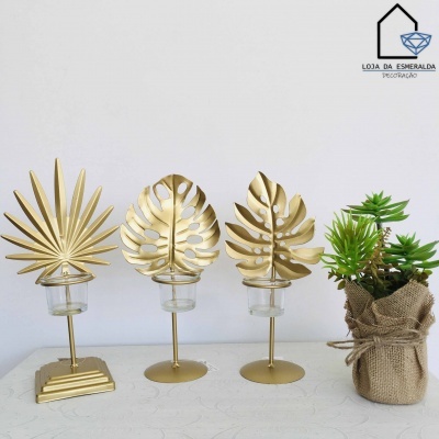 Três castiçais dourados com design de folhas tropicais e vaso com planta artificial em saco de juta