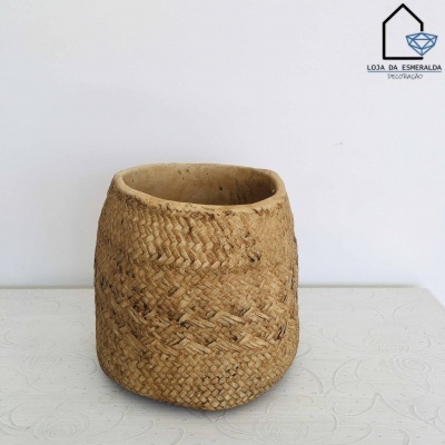 Cesto de palha trançada natural sobre mesa branca com textura, fundo branco e logotipo de loja