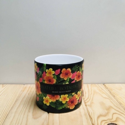 Vela em recipiente de cerâmica preto com decoração floral colorida e texto, sobre superfície de madeira.