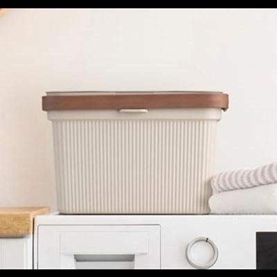 Caixa de arrumação plástica cinza com tampa castanha na máquina de lavar roupa branca com toalhas brancas e planta verde