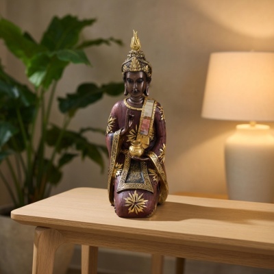 Estátua de Buda decorativa em madeira com dourado e vermelho numa mesa de madeira clara.