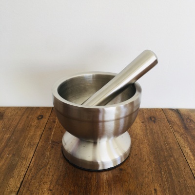 Pilão e almofariz de metal prateado sobre mesa de madeira