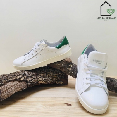 Ténis brancos com pormenores verdes sobre troncos de madeira