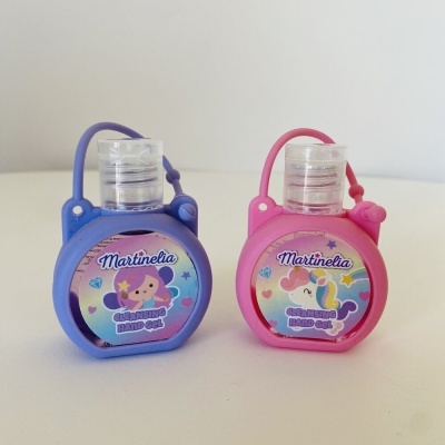 Dois frascos pequenos de gel desinfetante Martinelia com porta frascos em silicone azul e rosa.