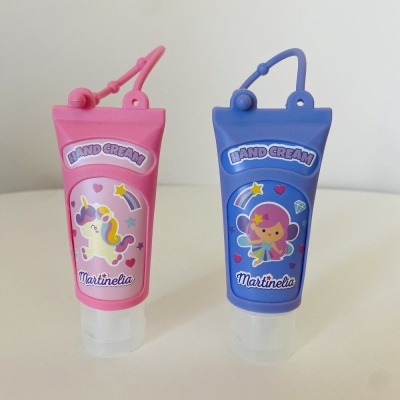 Duas embalagens coloridas de creme para mãos com argola, uma rosa com unicórnio e outra azul com fada.