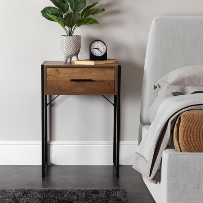 Mesa de cabeceira em madeira com vaso e relógio ao lado de cama cinzenta