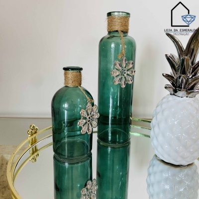 Frascos decorativos verdes em vidro com pendentes em padrão floral e base espelhada dourada ao lado de ananás decorativo branco e dourado