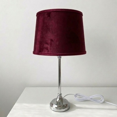 Candeeiro de mesa com base metálica prateada e cúpula em tecido vermelho vinho.