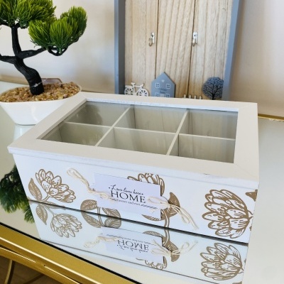 Caixa organizadora branca com tampa de vidro e divisórias, decoração de flores douradas e etiqueta decorativa.