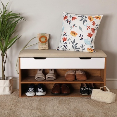 Banco organizador com assento almofadado bege, calçado, almofada floral e planta