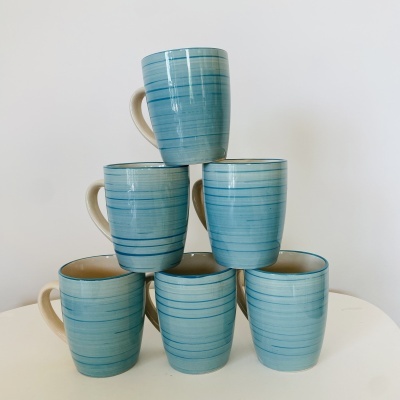 Seis canecas de cerâmica azuis com linhas horizontais em tons variados, dispostas em pirâmide sobre superfície branca