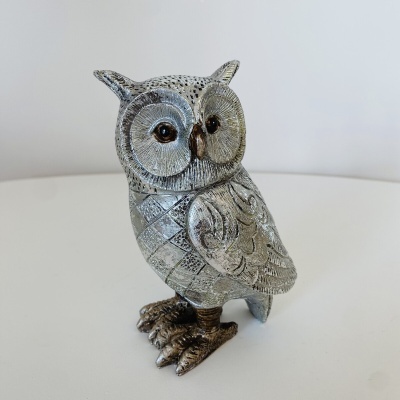 Estatueta de coruja metálica prateada com olhos castanhos em fundo branco