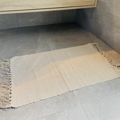 Tapete retangular bege claro com franjas colocado em chão de azulejos cinzentos