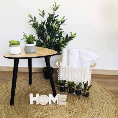Mesa redonda de madeira e preto com plantas e cesta branca com toalhas sobre tapete redondo de fibra