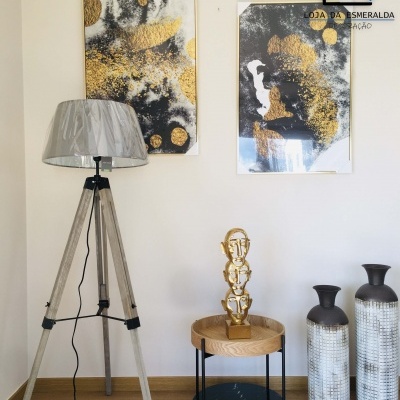 Decoração interior com abajur de tripé, mesa redonda, escultura dourada, jarros texturizados e quadros abstratos