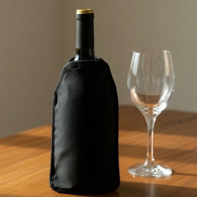 Garrafa protegida com capa preta ao lado de uma taça de vinho sobre mesa de madeira