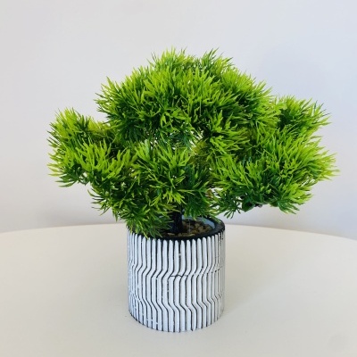 Planta artificial verde em vaso branco com padrão preto sobre superfície branca.