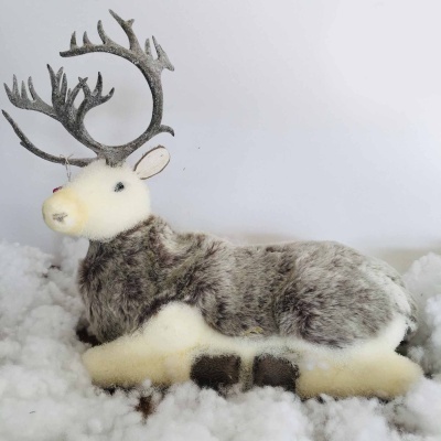 Rena decorativa felpuda cinzenta e branca com chifres, sobre superfície branca semelhante a neve