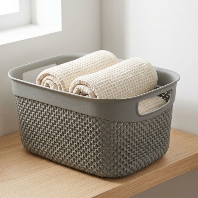 Cesto cinzento com três toalhas enroladas cor creme sobre superfície de madeira