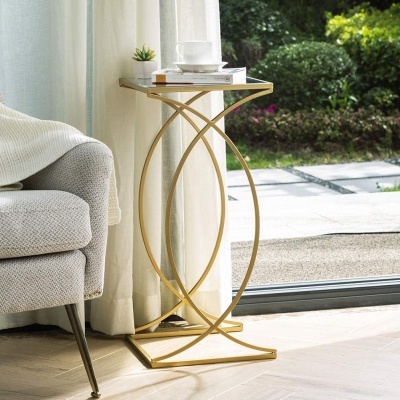 Mesa lateral dourada com tampo branco junto a sofá cinzento perto de janela com vista para jardim